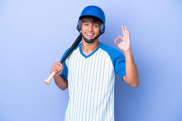 Baseball caucasian man player with helmet and bat isolated on blue background showing ok sign with fingers