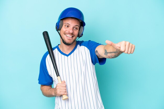 Baseball player with helmet and bat isolated on blue background giving a thumbs up gesture