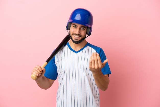 Baseball player with helmet and bat isolated on pink background inviting to come with hand. Happy that you came