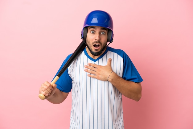 Бейсболист со шлемом и битой, изолированные на розовом фоне, удивлен и шокирован, глядя вправо
