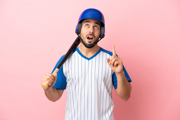 Baseball player with helmet and bat isolated on pink background thinking an idea pointing the finger up