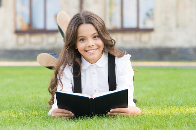 Basic education Extracurricular reading Cute small child reading book outdoors Adorable little girl learn reading Schoolgirl school uniform laying on lawn with favorite book Studying concept