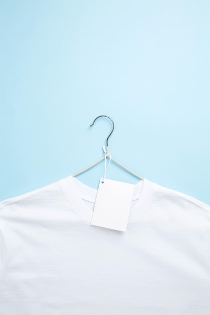 Basic wit t-shirt en hanger met witte papieren label blauwe achtergrond Bespotten voor branding tshirt Kopieer ruimte
