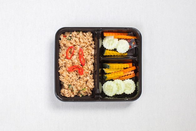 Basil fried rice with minced chicken, put in a black plastic box, put on a white tablecloth, food box, Spicy fried chicken with basil leaves, Thai food.