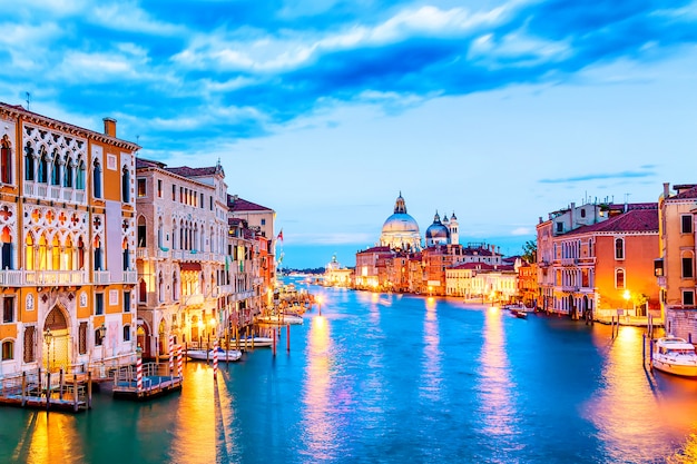 Basilica Santa Maria della Salute and Grand Canal at blue hour sunset in Venice, Italy with boats and reflections.