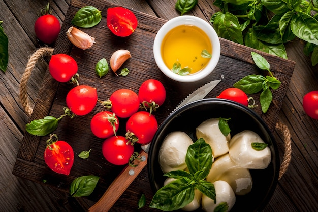 Basilicum, tomaten, mozzarellakaas, olijfolie op een oude houten tafel