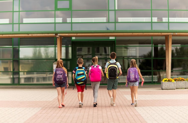 basisonderwijs, vriendschap, kindertijd en mensenconcept - groep gelukkige basisscholieren met rugzakken die buiten lopen van achteren