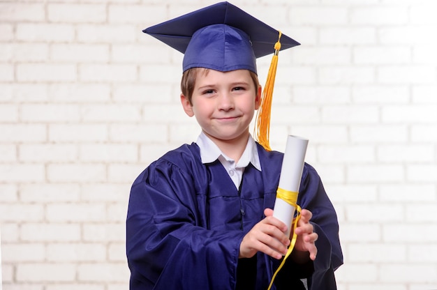 Basisschooljongen in kop en toga het stellen met diploma.