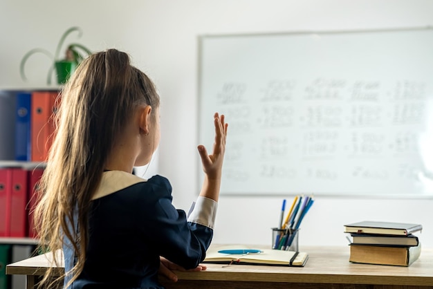 Basisschoolleerling steekt haar hand op omdat ze klaar is om de vraag van de leraar te beantwoorden