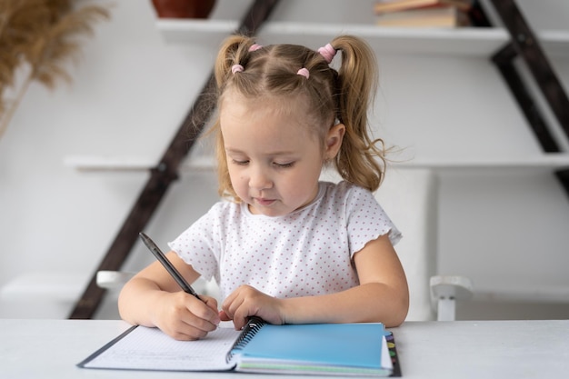 Basisschoolstudent kleuter die thuis studeert doet huiswerk met de hand geschreven in een notitieboekje of notitieblok zit aan een bureau De kleuter leert online op afstand Onderwijs op afstand