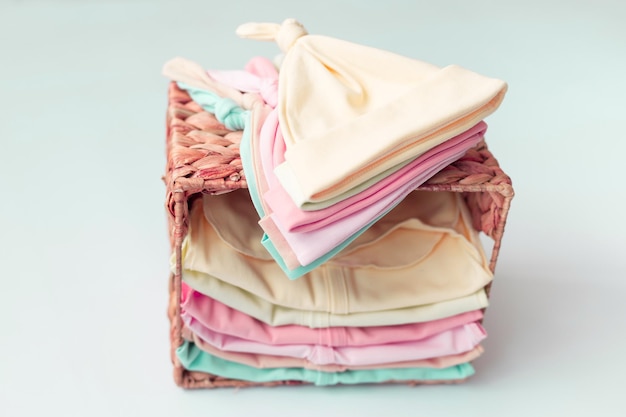 A basket of baby clothes with a pink hat on top