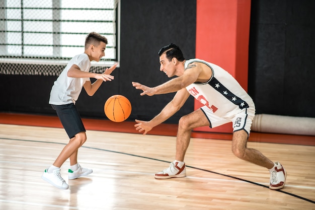 Баскетбол. Темноволосый мужчина тренирует подростка в спортзале