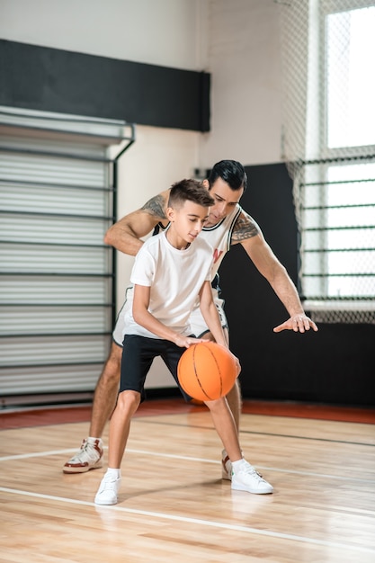 Basket-ball. Dark-haired man training a teen in the gym