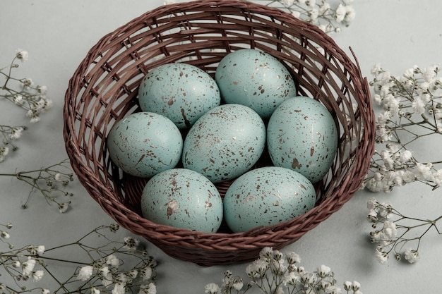 A basket of blue eggs sits on a table with flowers and a white flower.