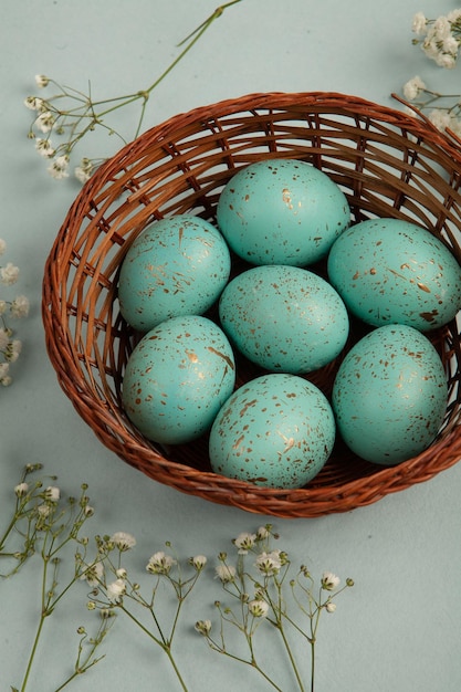 A basket of blue eggs with a bunch of flowers on the side.