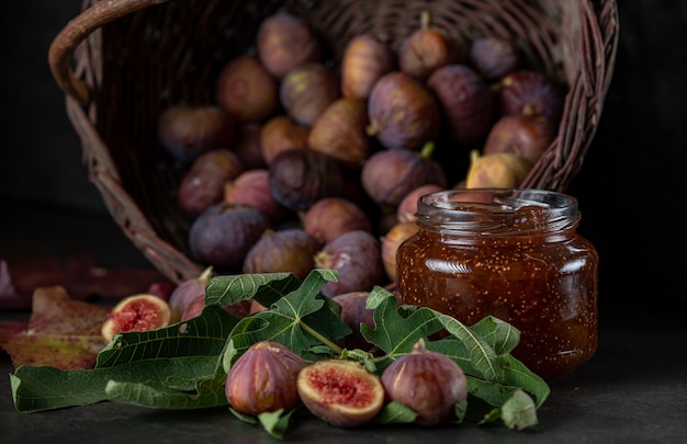 A basket of fresh figs and a jar of fig jam on a dark gray background