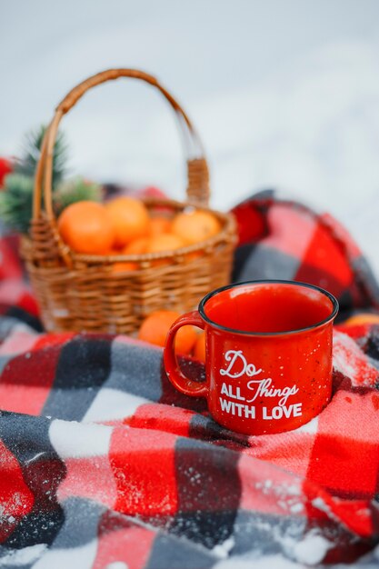 雪の中のオレンジのバスケット、お茶のマグカップ、赤い毛布