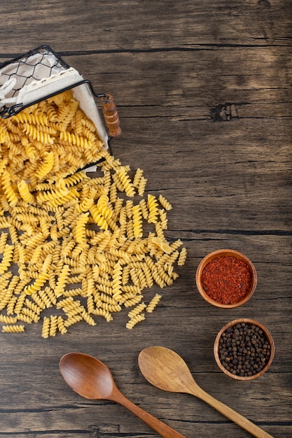 Basket of raw fusilli pasta with pepper spices on wooden table. 