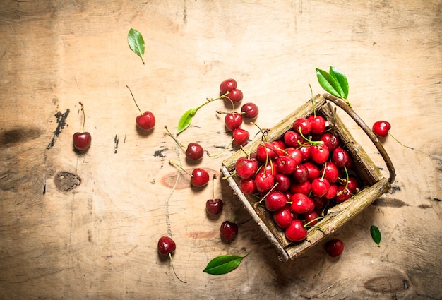 Basket of red cherry and leaves . On a wooden table.