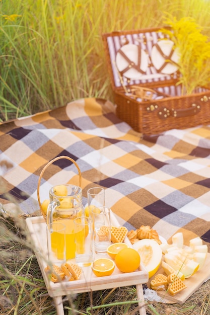 A basket and a table with fruits and pastries at a picnic in summer in the rays of sunset light