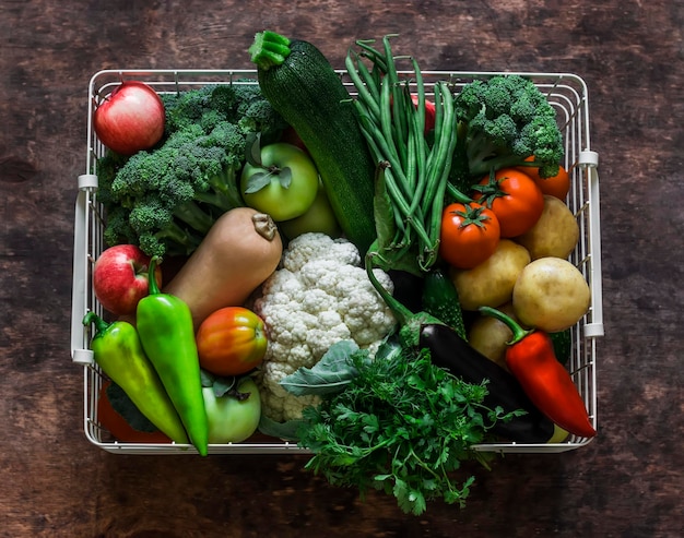 Basket with an abundant autumn seasonal harvest of vegetables pumpkin cauliflower broccoli string beans squash potatoes tomatoes on a wooden background top view