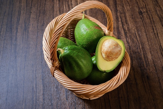 Basket with avocados on wooden table. Basket with avocados and one avocado cut in half.