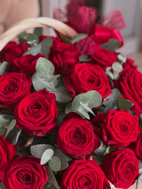 꽃집의 의자에 밝은 빨간 장미와 유칼립투스가 있는 바구니. 휴가를 위한 아름다운 꽃다발. 엽서의 배경
