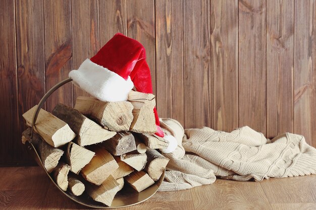 Basket with firewood and Santa Claus hat on wooden background