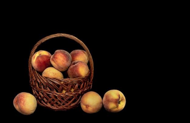 Photo basket with a harvest of ripe peaches on a black background