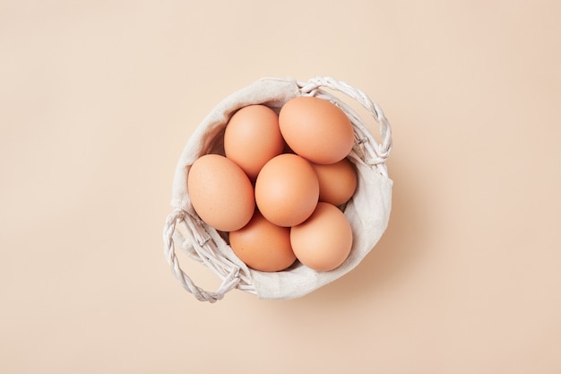 Корзина с домашними яйцами по центру картинки на бежевом фоне