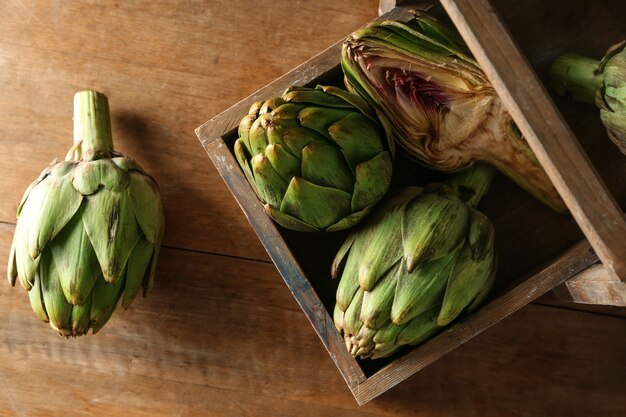 Basket with raw artichokes on wooden table