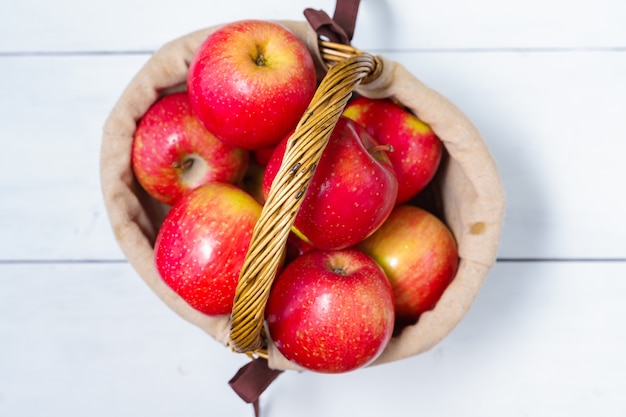 Basket with ripe red social apples on white wooden background