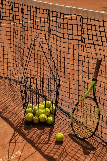 Basket with tennis balls and racket against net on clay court