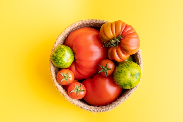 Basket with a variety of tomatoes, including: Cherry, Heirloom and Zebra on a yellow background