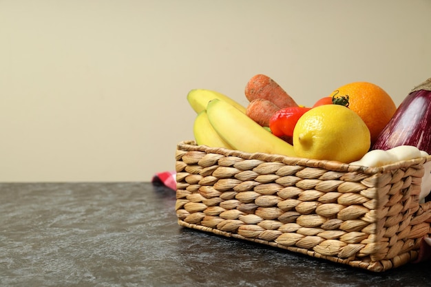 Basket with vegetables and fruits on kitchen towel on black smokey table