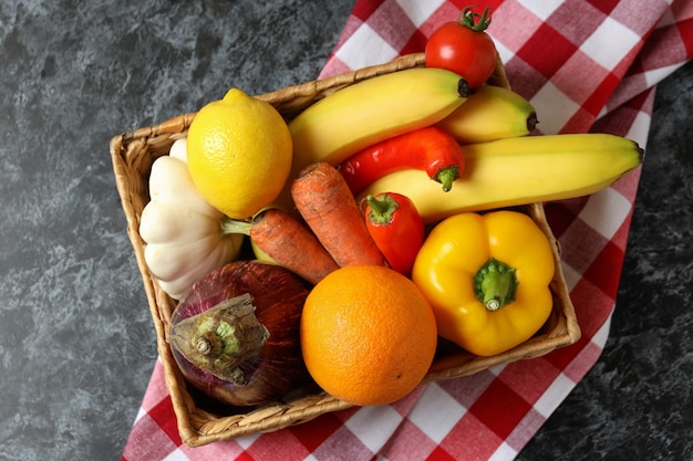 Basket with vegetables and fruits on kitchen towel on black smokey table