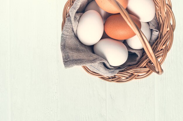 Basket with white and brown natural eggs on white wooden background