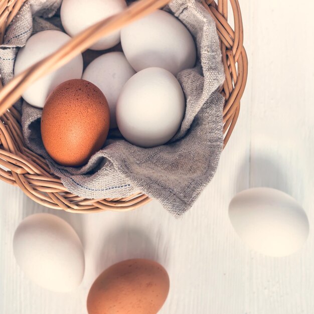 Basket with white and brown natural eggs on white wooden background