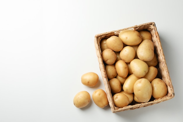 Basket with young potatoes on white surface