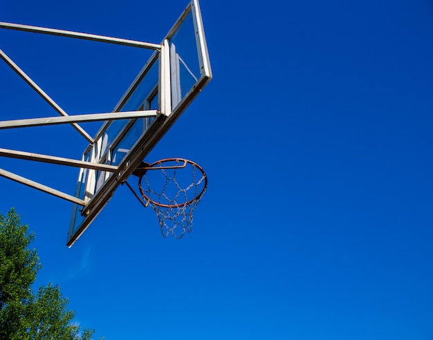 空を背景に遊び場の路上にリングが付いたバスケットボールのバックボード