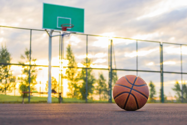 A basketball ball lies on the ground in the background of a shield and an evening sky