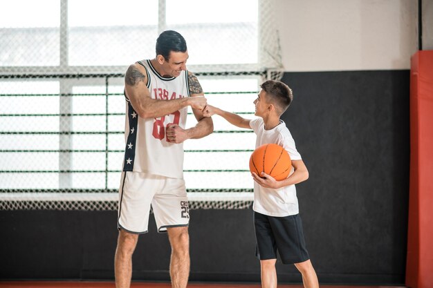 Basketball. Coach in white sportswear teaching the boy playing basketball