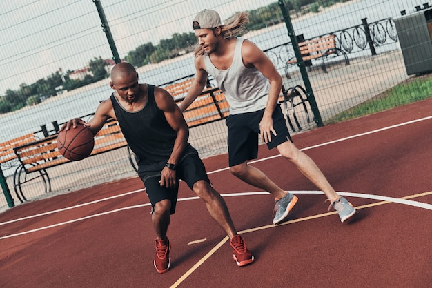 Фото Баскетболисты. двое молодых людей в спортивной одежде играют в баскетбол, проводя время на открытом воздухе