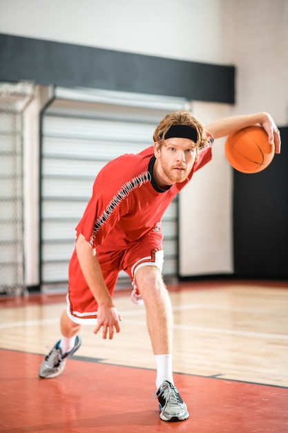バスケットボール。バスケットにボールを投げる赤いスポーツウェアの生姜男