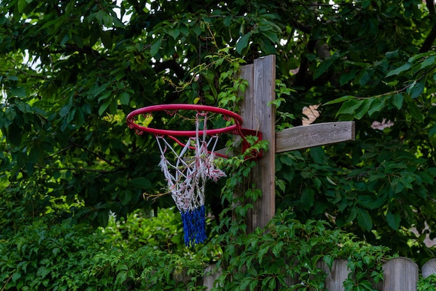 Баскетбольное кольцо прибито к деревянному забору в загородном дворе порванной сеткой