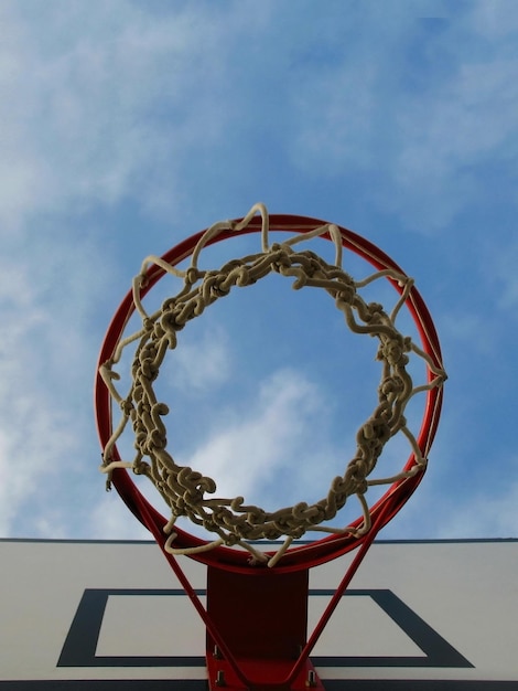 Basketball hoop with net on an outdoor court with sky and\
clouds background