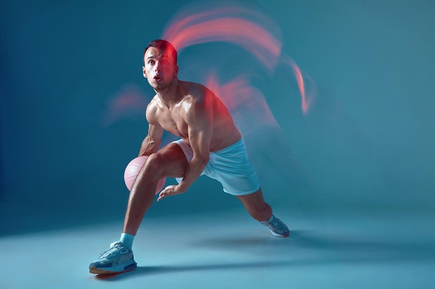 Basketball player athletic modern male dribbling ball with naked torso in neon light long exposure