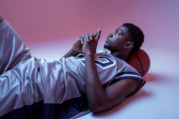 Basketball player lying with ball. Professional male baller in sportswear playing sport game, tall sportsman