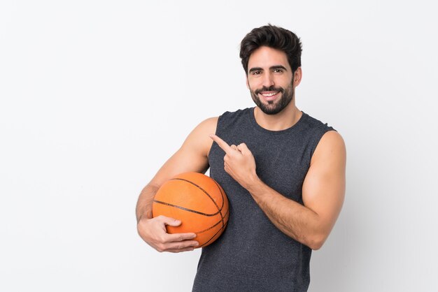 Uomo del giocatore di pallacanestro con la barba sopra la parete bianca isolata che indica il lato per presentare un prodotto