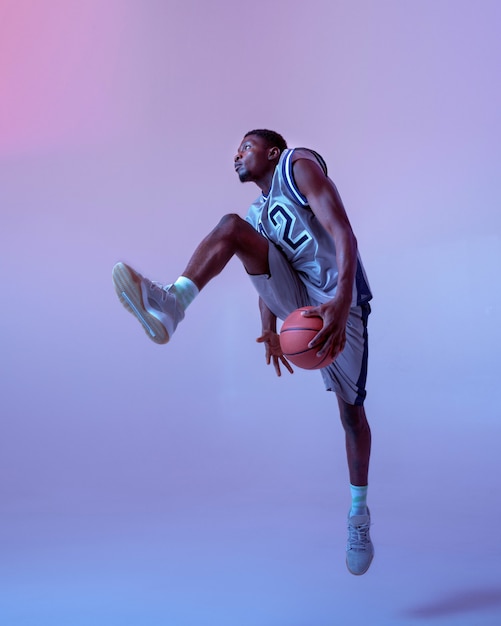 Basketball player moving with ball in studio, neon background. Professional male baller in sportswear playing sport game, tall sportsman